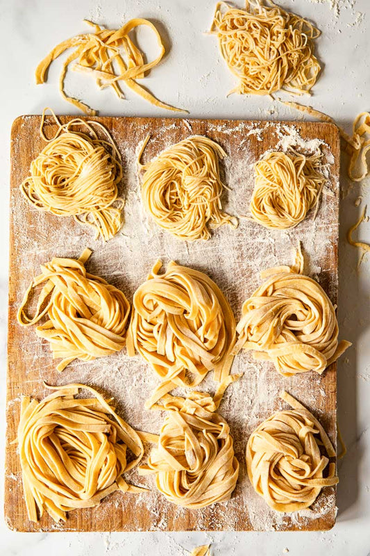 11 Nests of Homemade Pasta on a Floured Wooden Chopping Board
